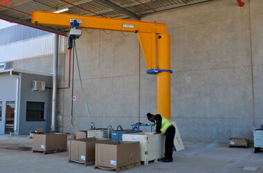 Pillar slewing jib crane outside the warehouse for loading machine components